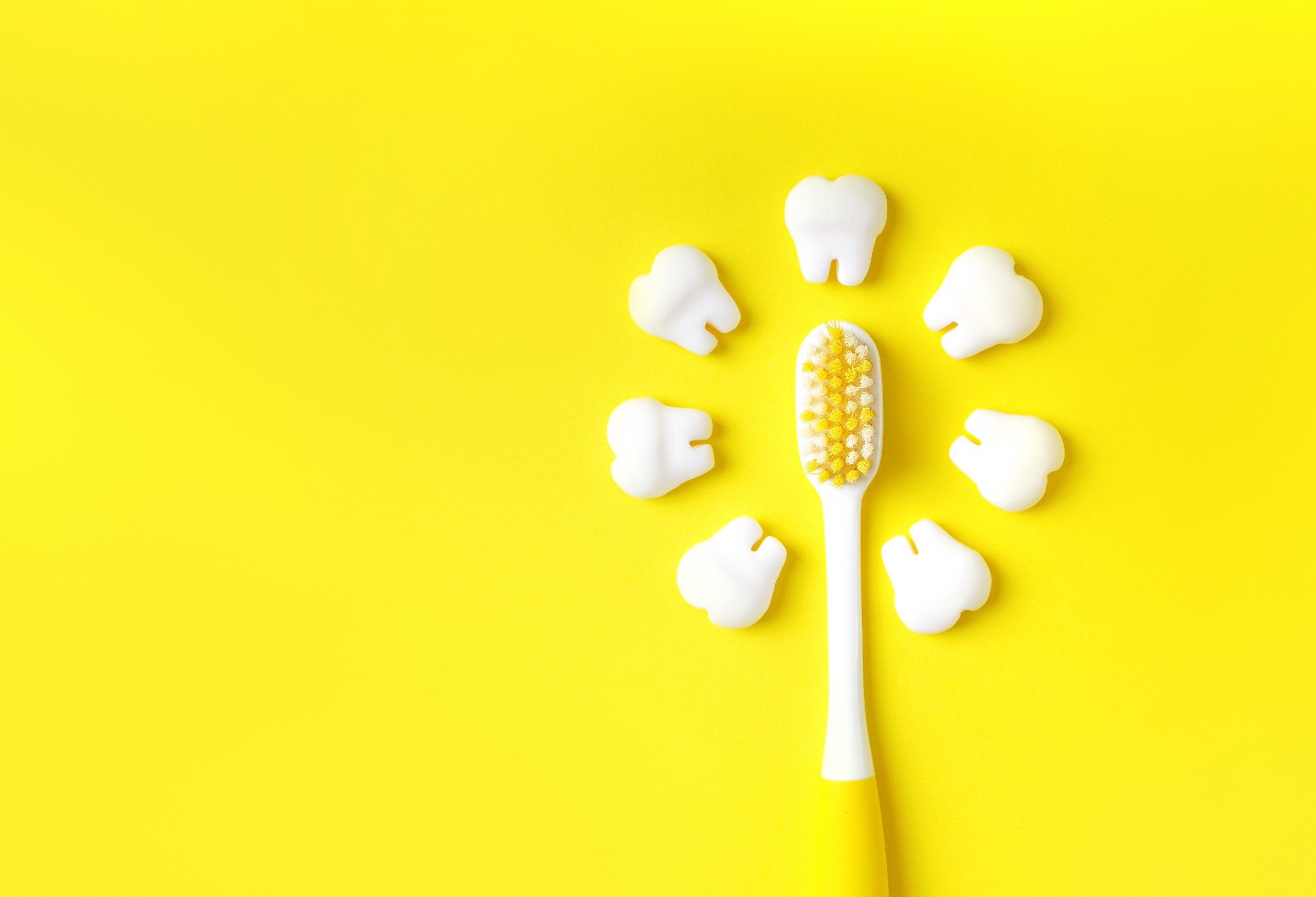 Toothbrush with teeth models making sun on a yellow background. Copy space.